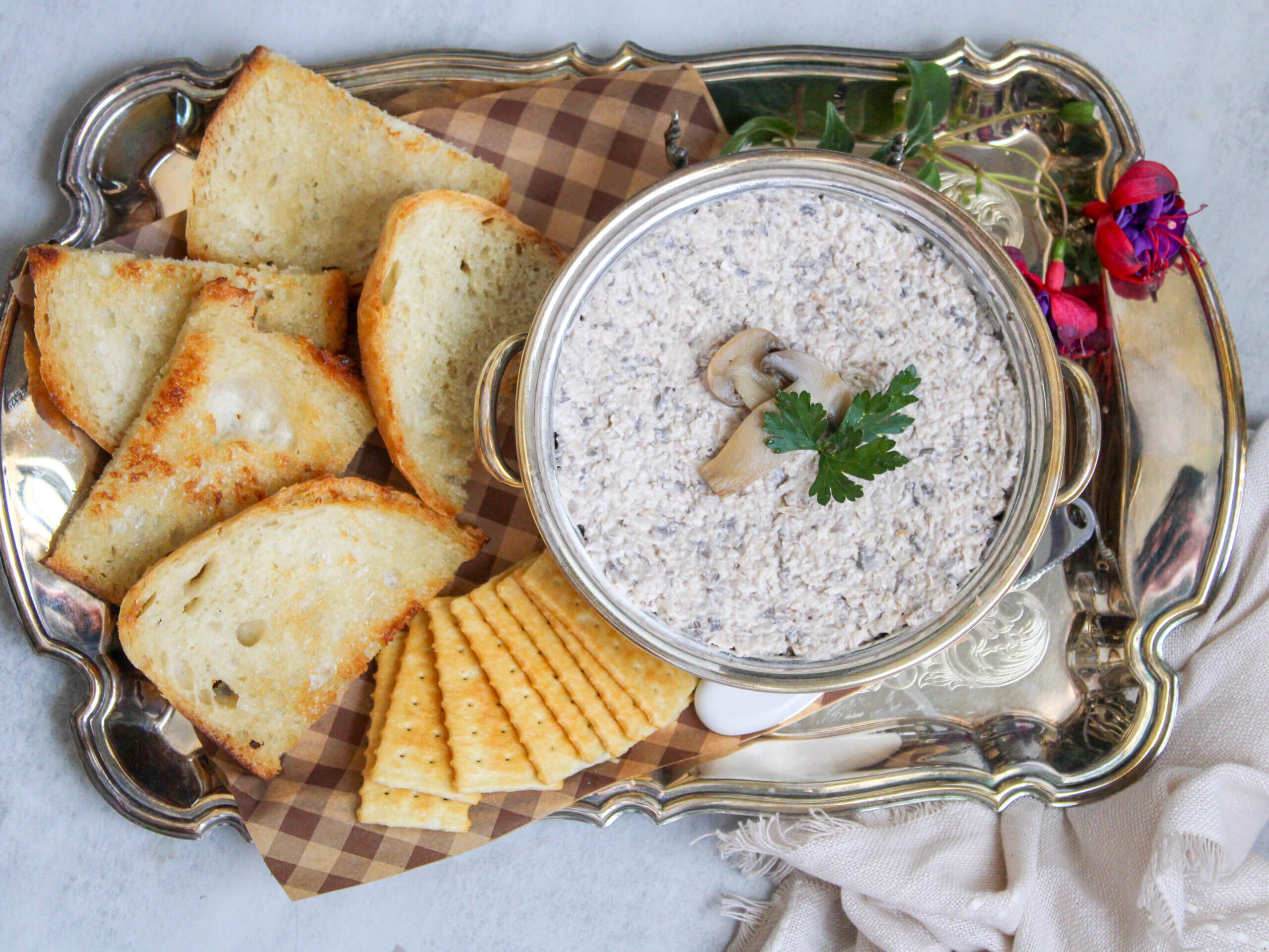 Creamy homemade Russian mushroom spread made with cremini mushrooms, walnuts, garlic, and mayonnaise served with toasted bread and crackers on a silver serving tray.