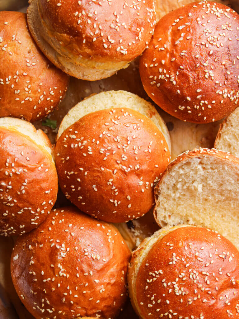 Freshly baked homemade hamburger buns topped with sesame seeds, featuring a soft, fluffy interior and golden brown bakery-style crust.