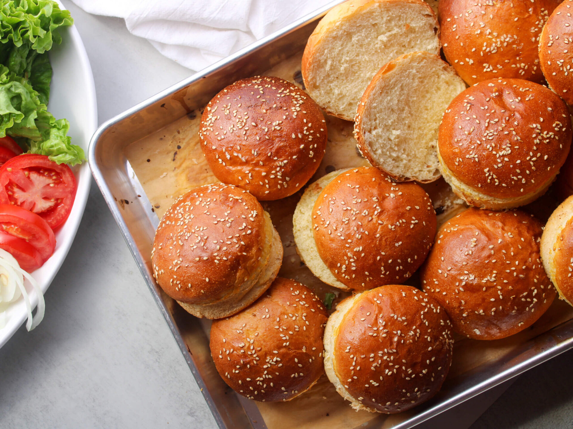 Homemade sesame hamburger buns with a soft, fluffy interior on a baking tray.