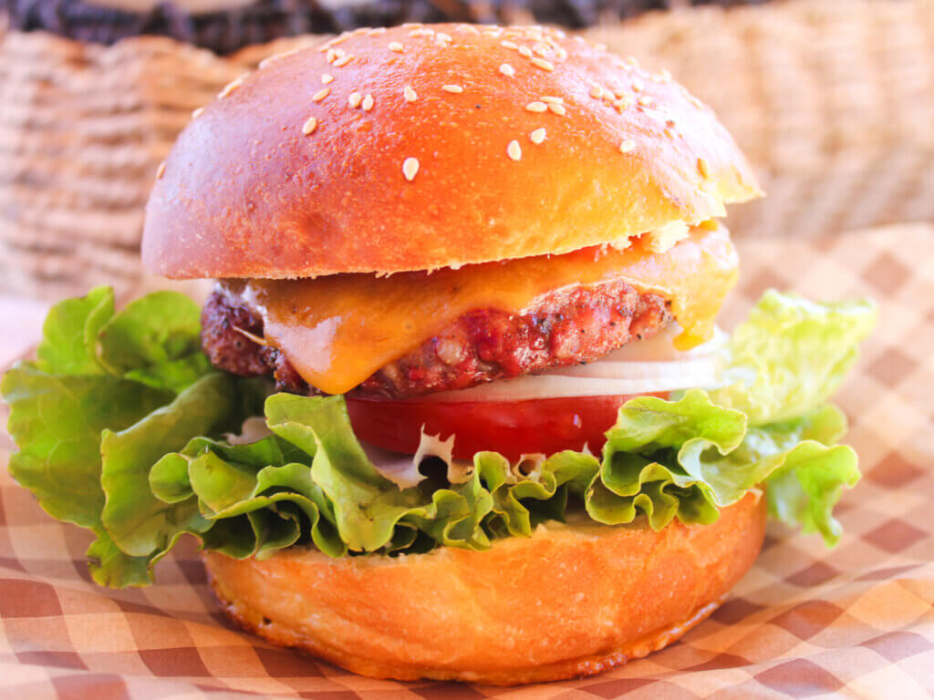 Juicy homemade cheeseburger on a soft sesame hamburger bun with fresh lettuce, tomato, onion, and melted cheddar cheese, made with homemade burger buns.
