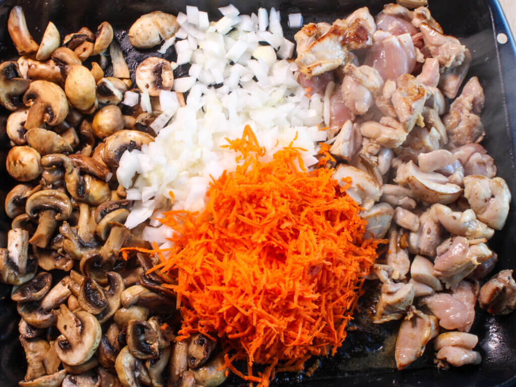 Chicken thighs, sliced mushrooms, chopped onions, and grated carrots sautéing in butter to make creamy mushroom chicken with potatoes.