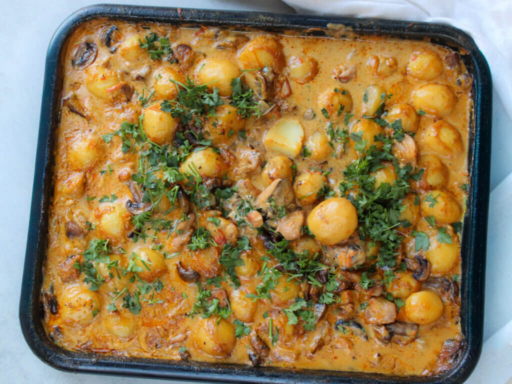 Creamy mushroom chicken with potatoes baked in a roasting pan, featuring tender chicken thighs, baby potatoes, mushrooms, and a rich homemade cream sauce topped with fresh parsley.