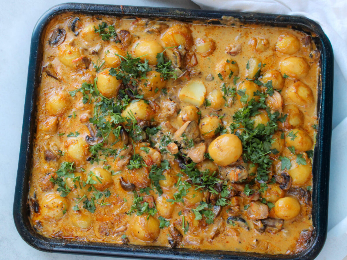 Creamy mushroom chicken with potatoes baked in a roasting pan, featuring tender chicken thighs, baby potatoes, mushrooms, and a rich homemade cream sauce topped with fresh parsley.
