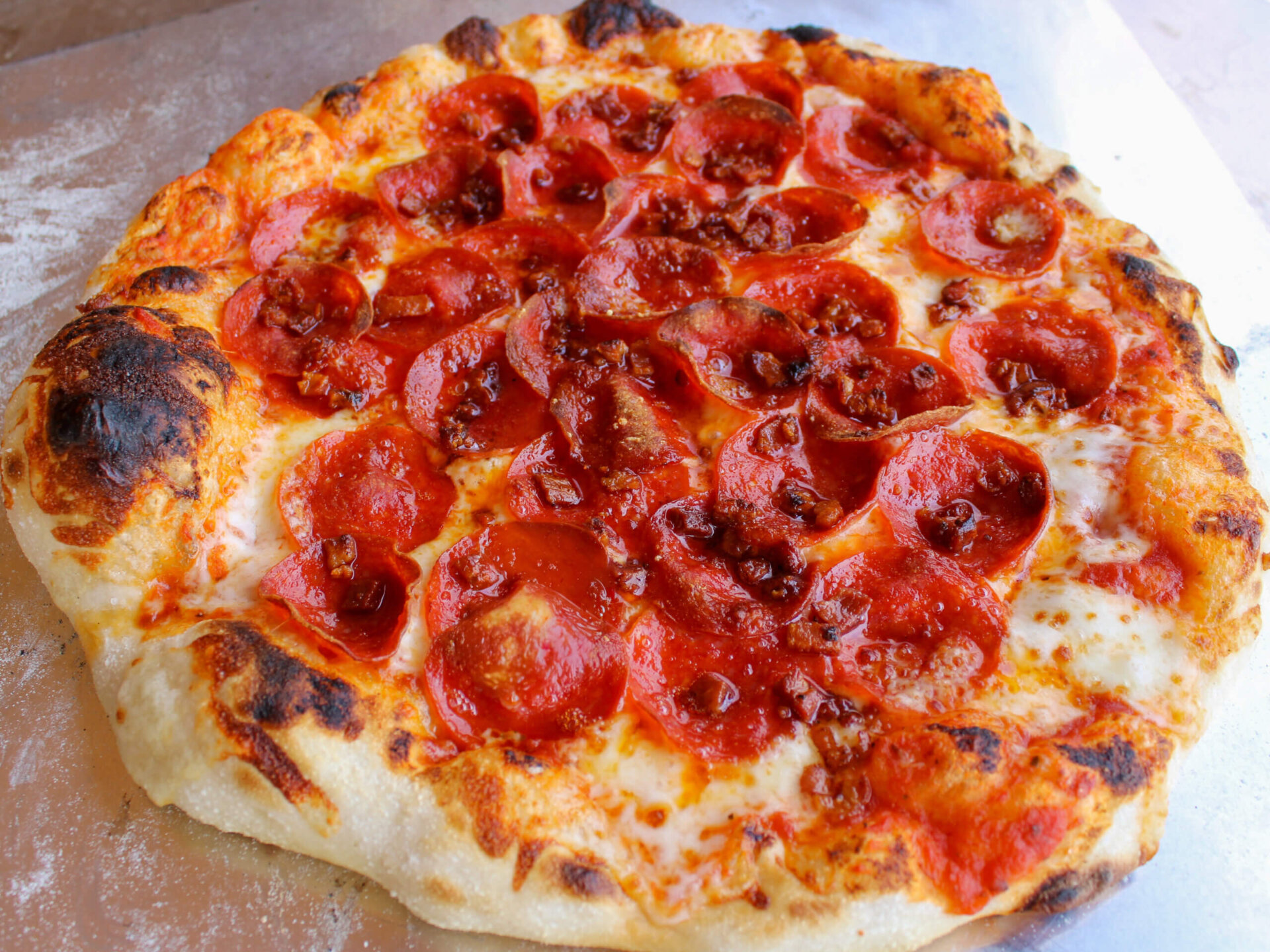 Homemade pepperoni pizza with a big airy crust, bubbly edges, melted mozzarella, and crispy pepperoni baked in a pizza oven.